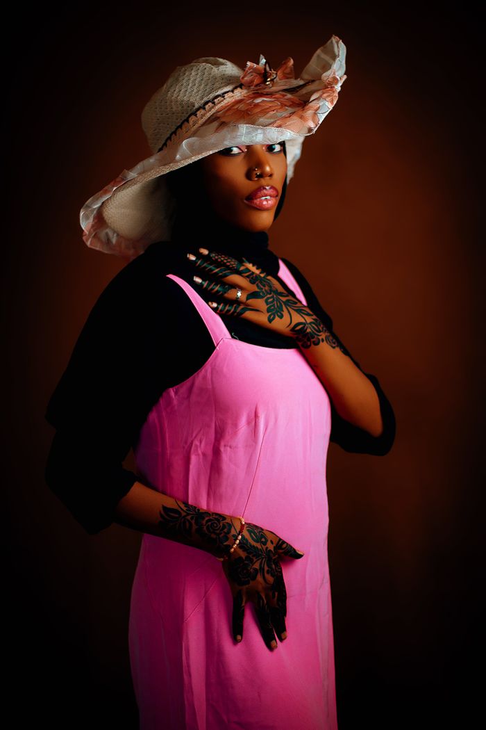 Stylish woman in pink dress and hat with intricate henna designs, exuding elegance.